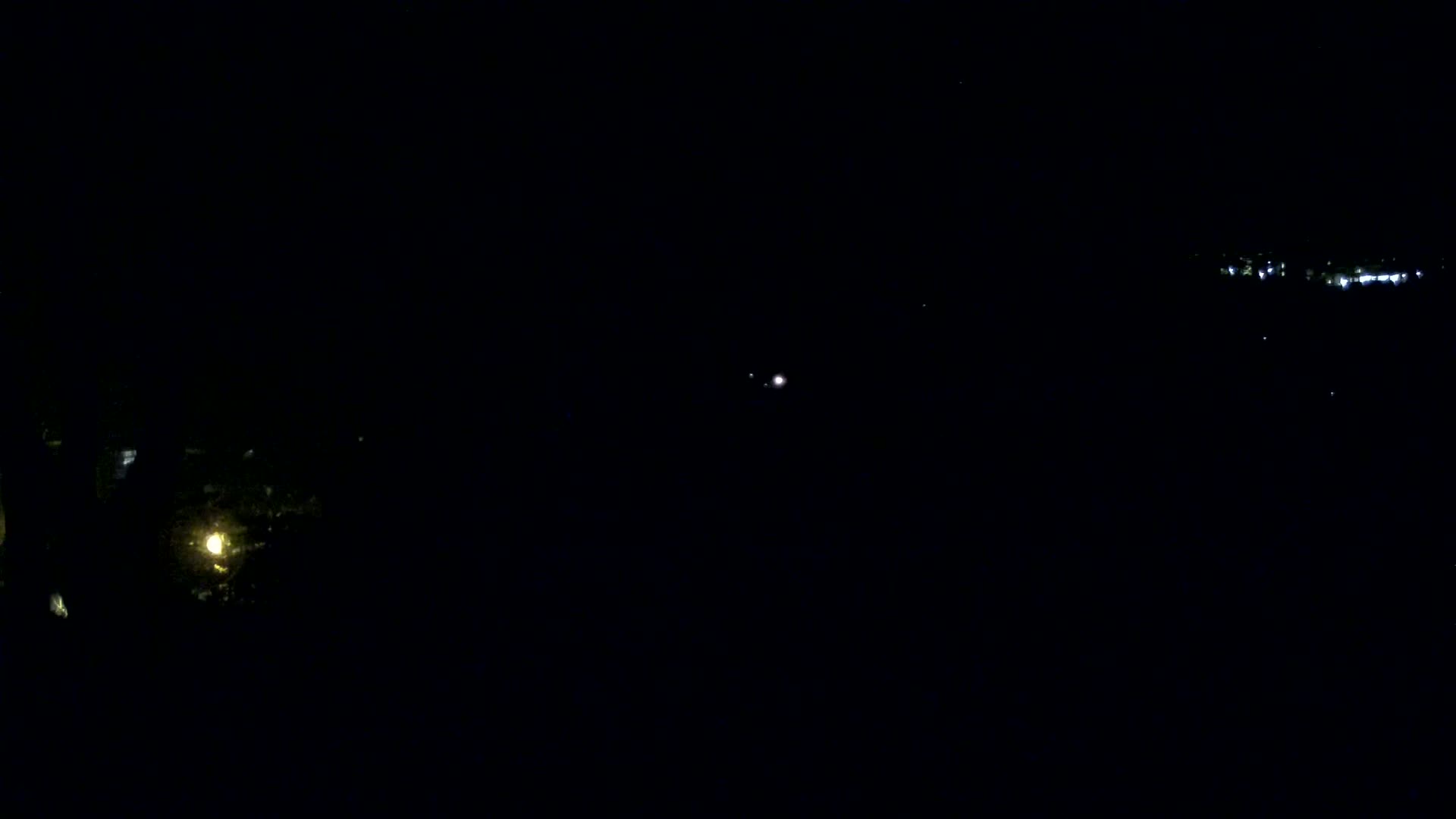 A nighttime view shows a small, illuminated area in the lower left and a larger expanse of lights in the distance on a clear night.