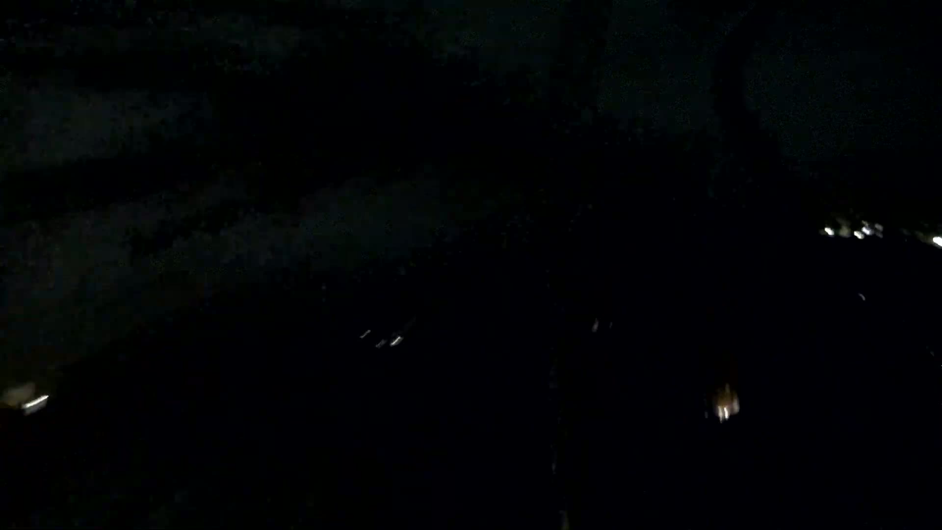 A dark, nighttime scene shows faintly illuminated distant structures and what appears to be light snowfall or dust.