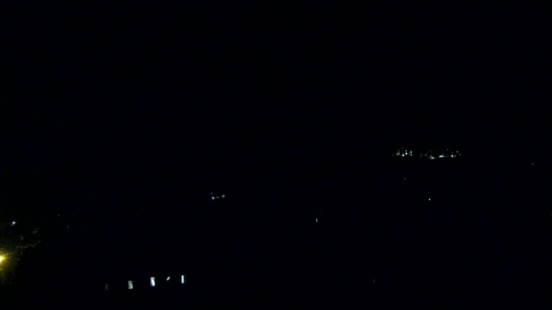 A nighttime, long-distance view shows faintly illuminated buildings and a few scattered lights in the dark.