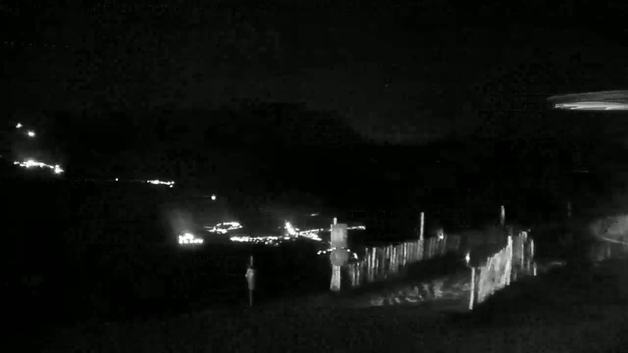 A nighttime, low-light view shows a distant line of lights, possibly from a town or road, beyond a short fence and dark foreground.