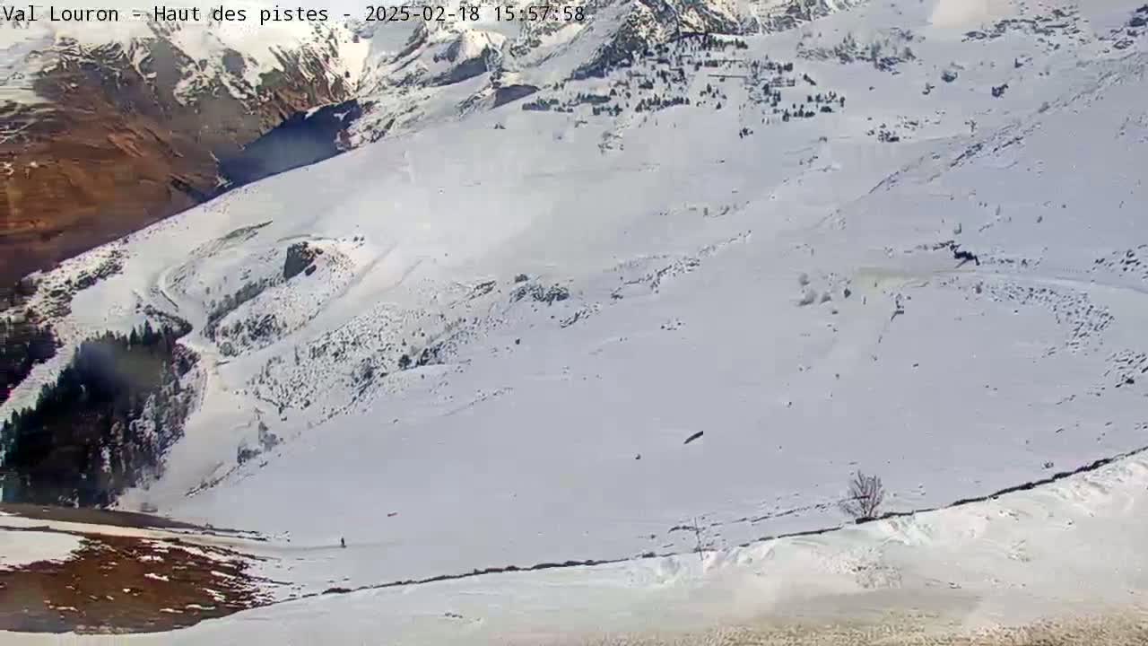 A snow-covered mountain slope with a few skiers visible, under a bright, sunny sky.