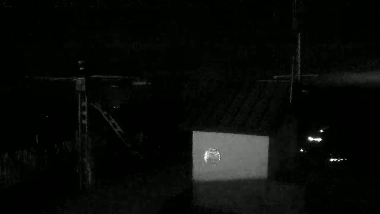 A low-light, nighttime image shows a partially illuminated, flood-covered building and some structures, possibly utility poles, under a dark sky.