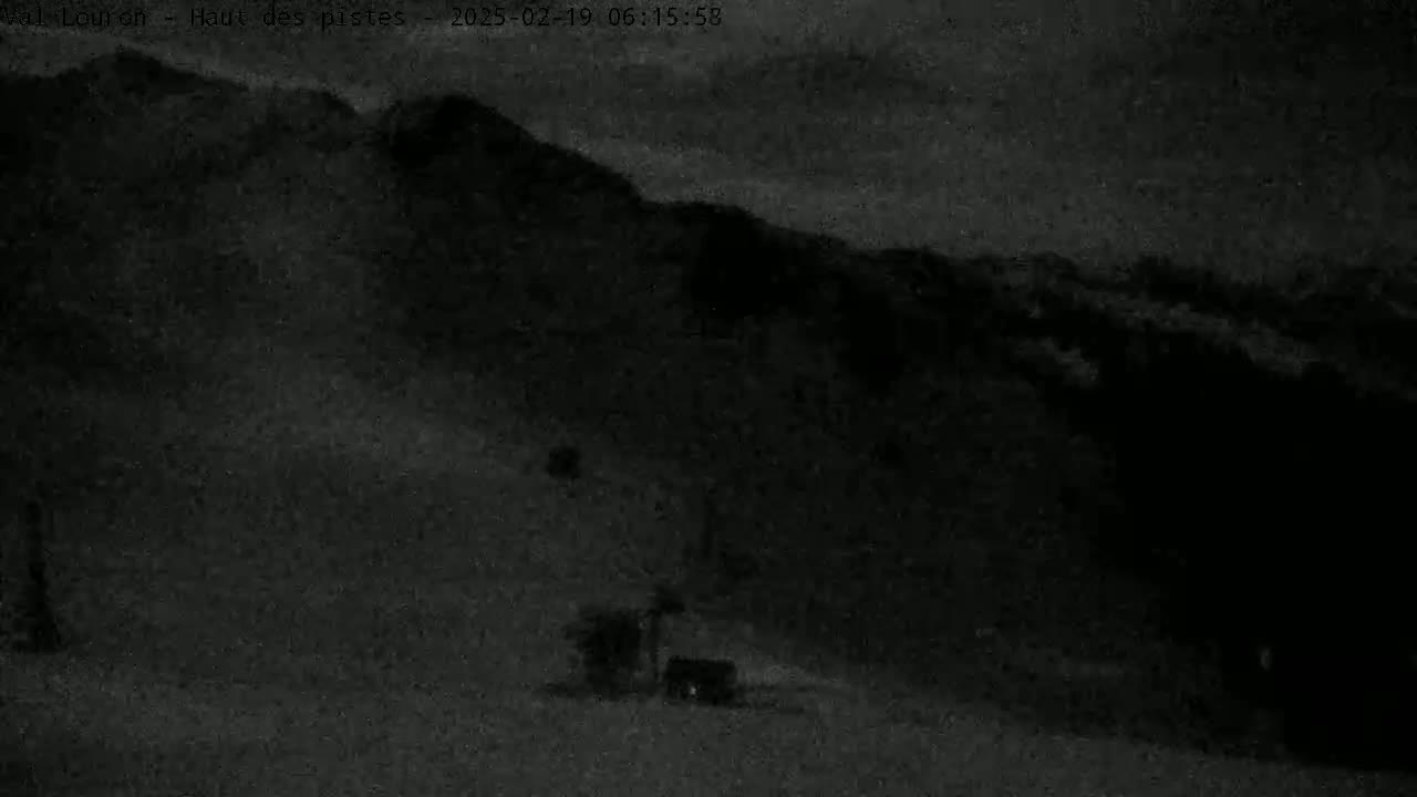 A dark, nighttime image shows a snow-covered hillside with a few indistinct objects near the bottom.