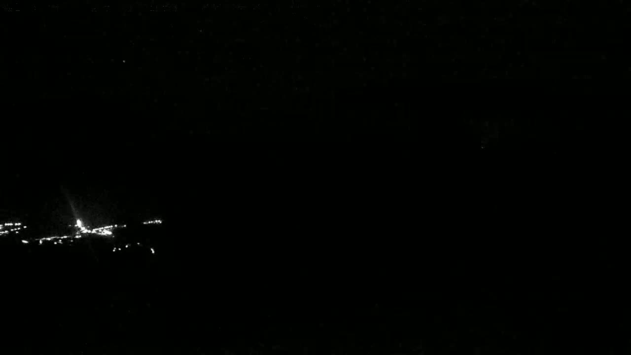 A low-light nighttime image shows a line of distant lights at the bottom of the frame.