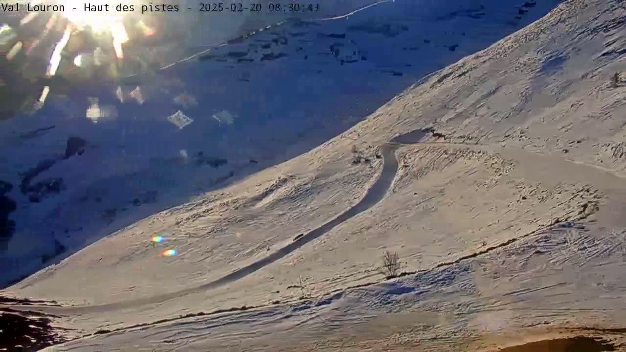 A snow-covered mountain slope with a winding path is visible under a bright, sunny sky.