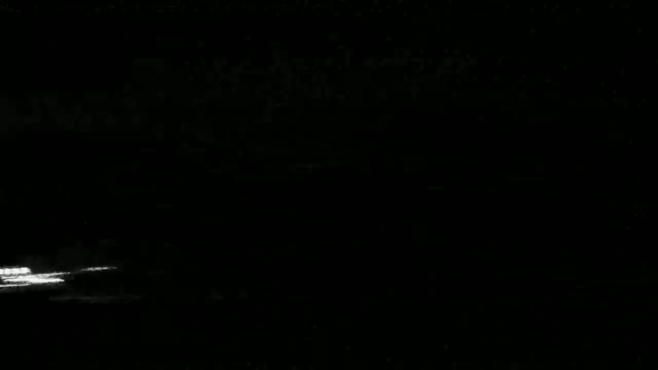 A dimly lit nighttime scene shows a faint, bright horizontal line near the bottom, possibly reflecting light on water.