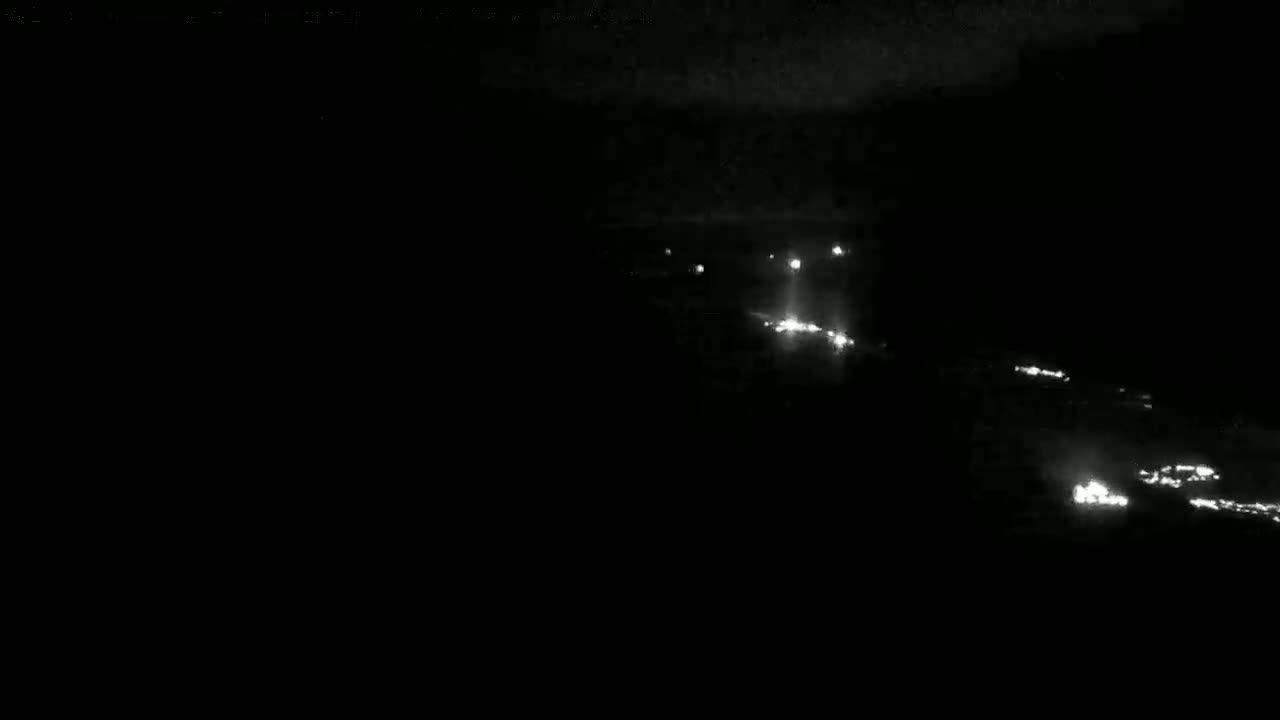 At night, a long line of vehicle headlights are visible in the distance.