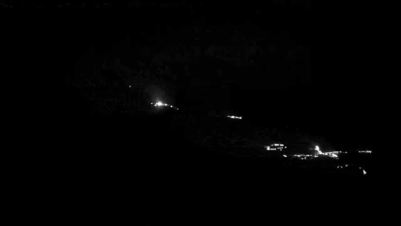 A nighttime long shot shows a series of small, scattered lights on a dark, possibly hilly landscape.