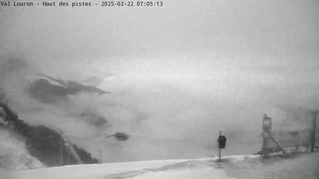 A snow-covered landscape is obscured by heavy fog or blowing snow, with indistinct mountainous features in the background.