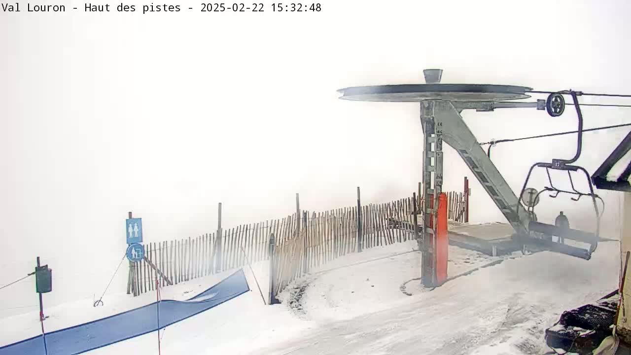A ski lift chair hangs at a snow-covered station in heavy fog.
