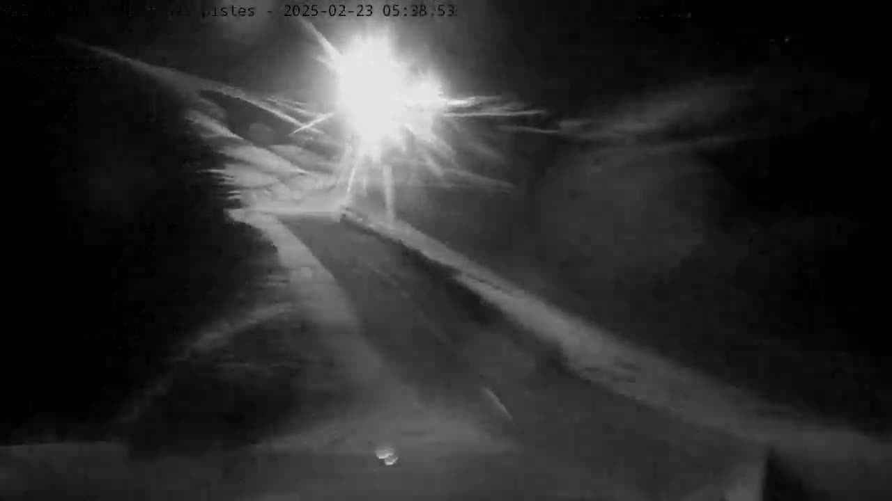 A bright light shines through heavy nighttime snow clouds over a dark, snow-covered slope.