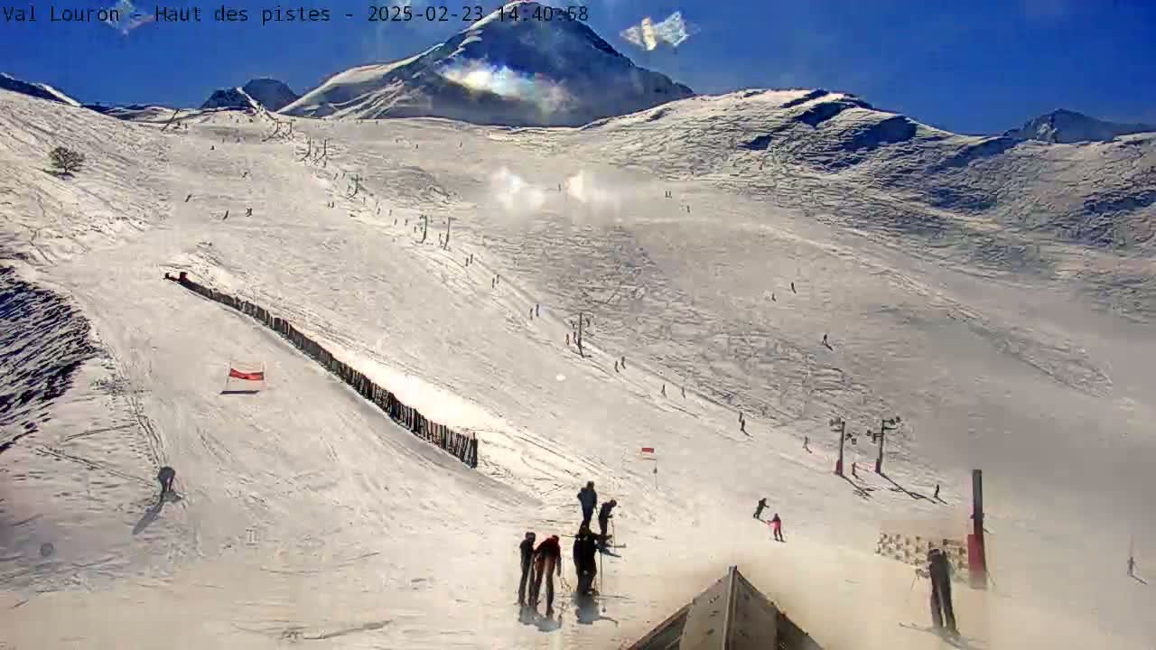 A snow-covered ski slope with several skiers and snowboarders descending under a clear, sunny sky.