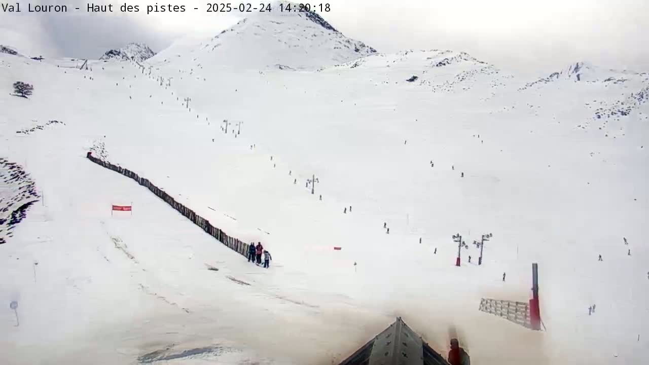 A snowy mountain slope with several skiers and snowboarders visible, under overcast skies.