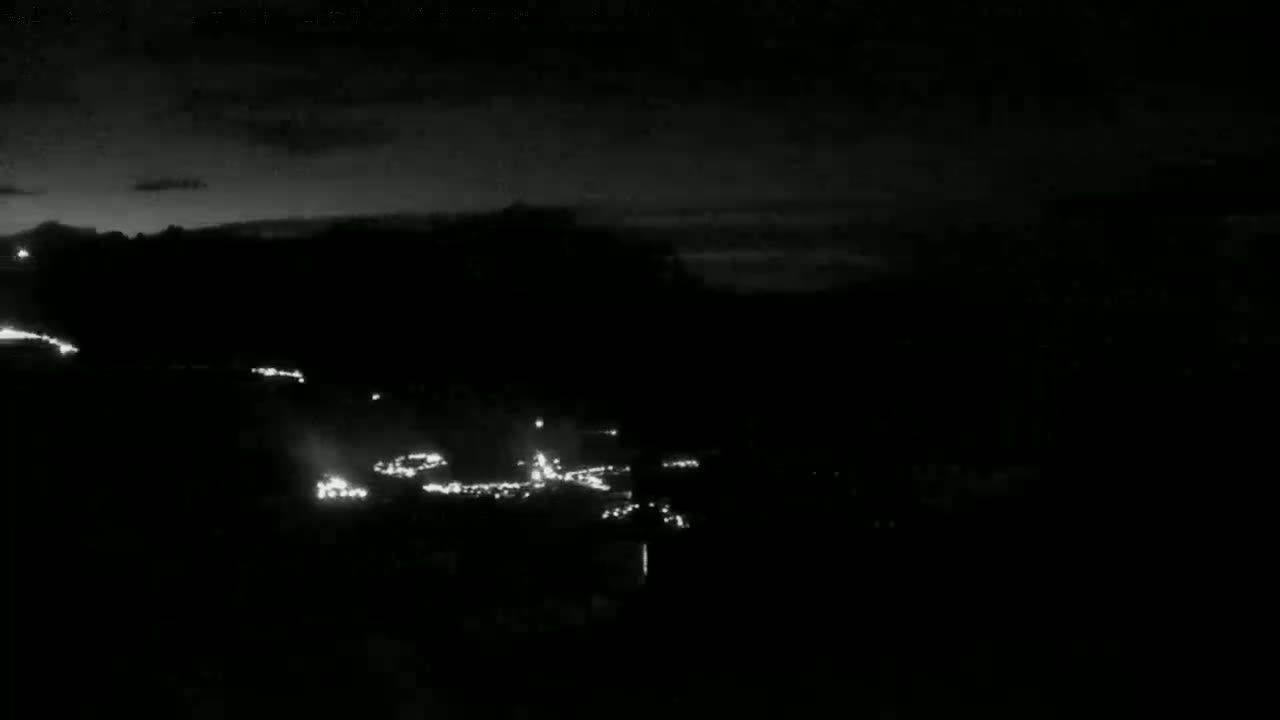 A nighttime long shot shows a dark landscape with a string of distant lights possibly from vehicles on a road or town.