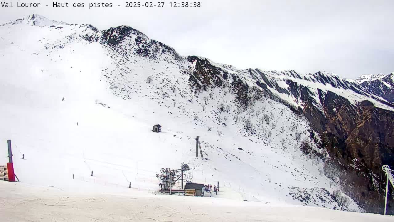 A snow-covered mountain slope with a ski lift and several skiers visible under an overcast sky.