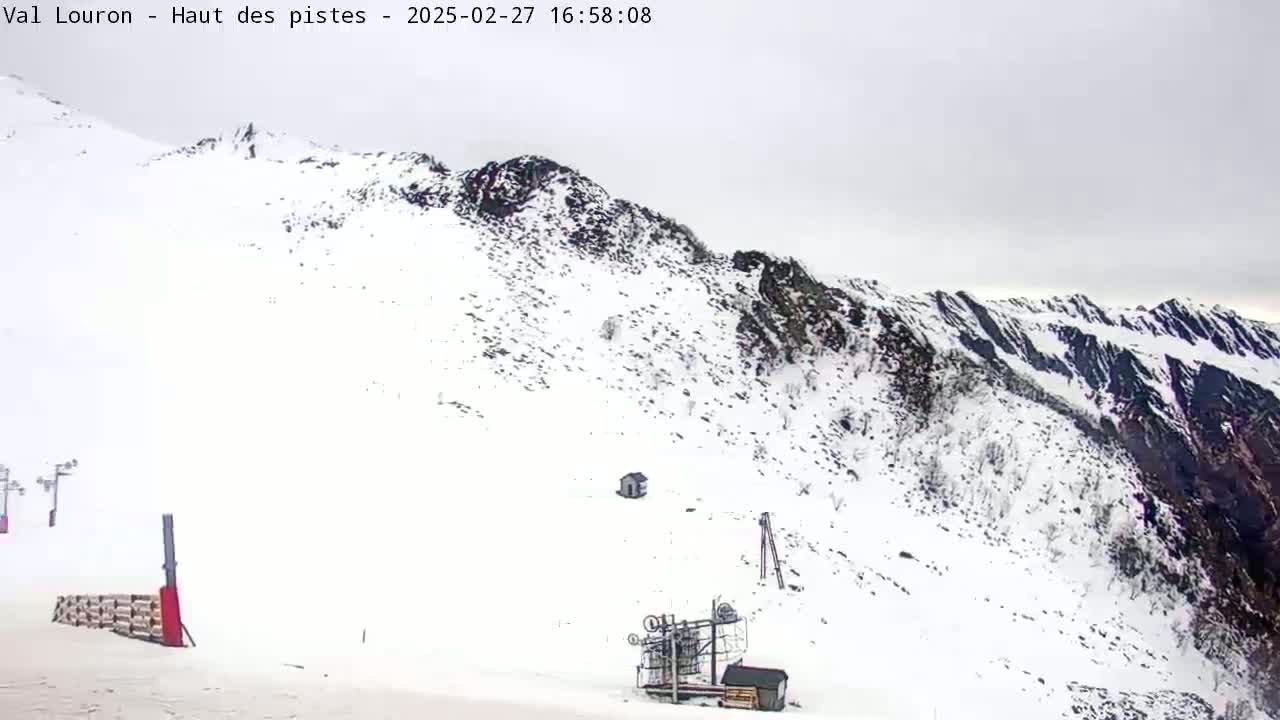 A snow-covered mountain slope is shown on an overcast day, with ski lift equipment visible in the foreground.