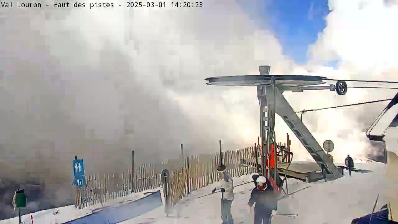 A ski lift in snowy conditions with blowing snow obscuring the view, and several people standing near it.