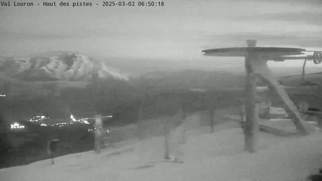 A snowy, overcast mountain landscape is visible from a ski lift, with a distant town illuminated below.