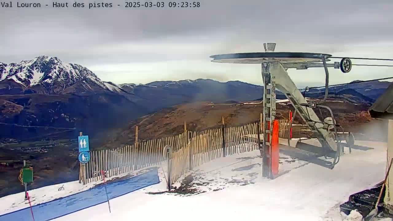 A snow-covered ski lift station overlooks a mountain range under an overcast sky.