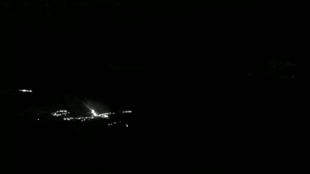 A nighttime, low-light view shows a lightning strike illuminating a dark landscape with sparsely scattered lights.