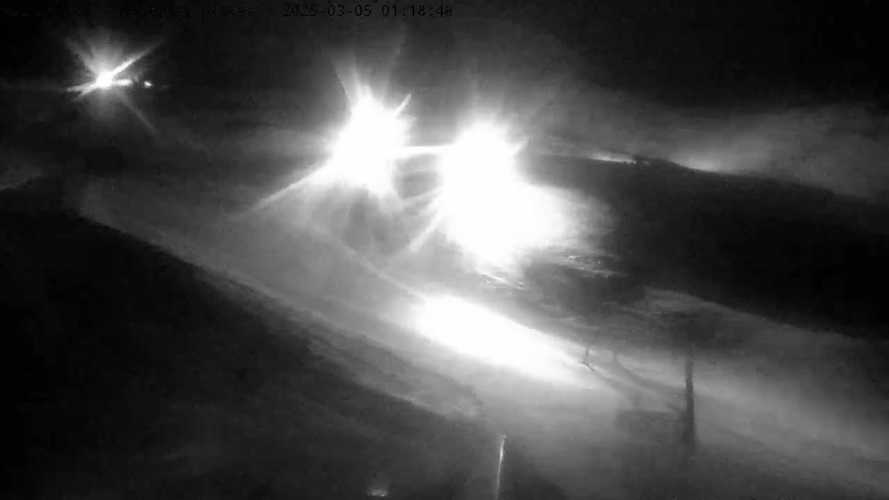 At night in snowy conditions, the bright headlights of two vehicles are visible on a road.
