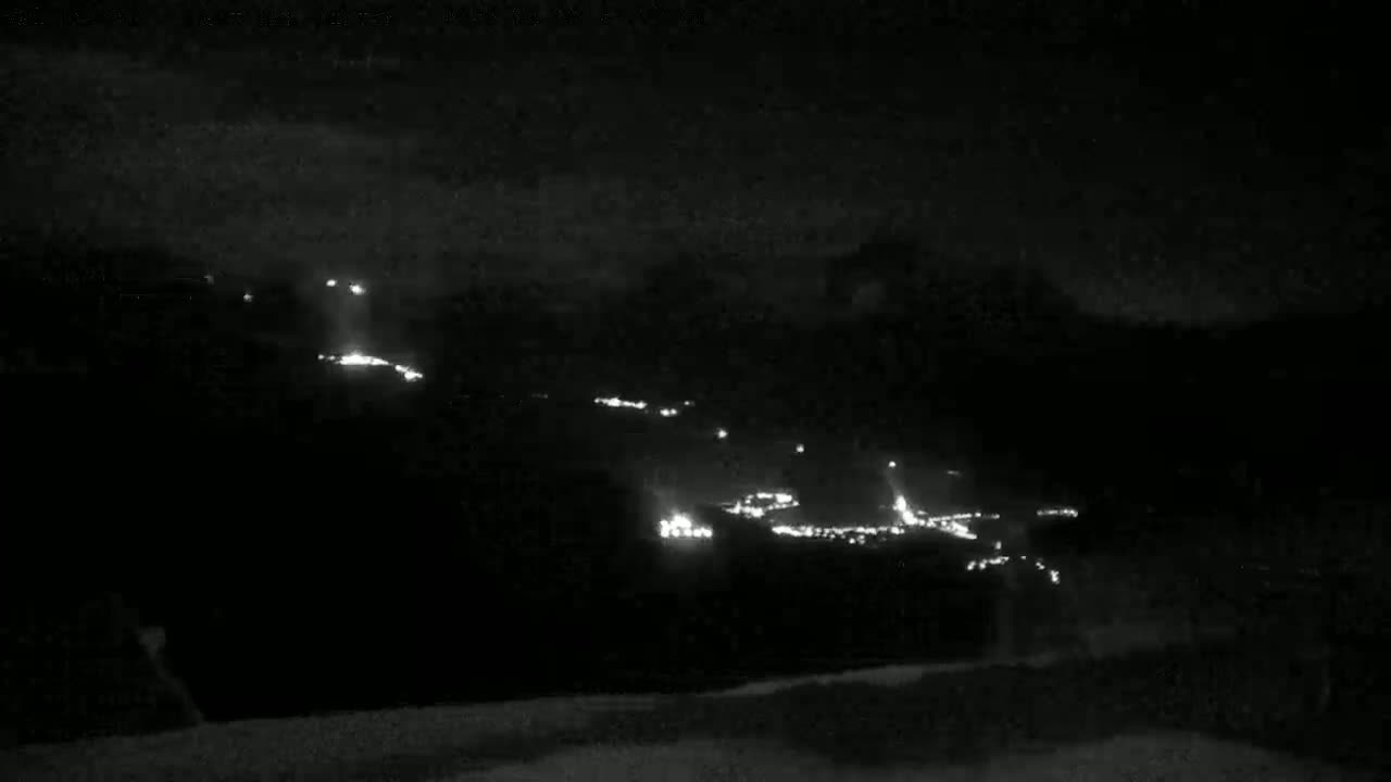 At night, a line of headlights from vehicles is visible on a dark road winding up a hill.