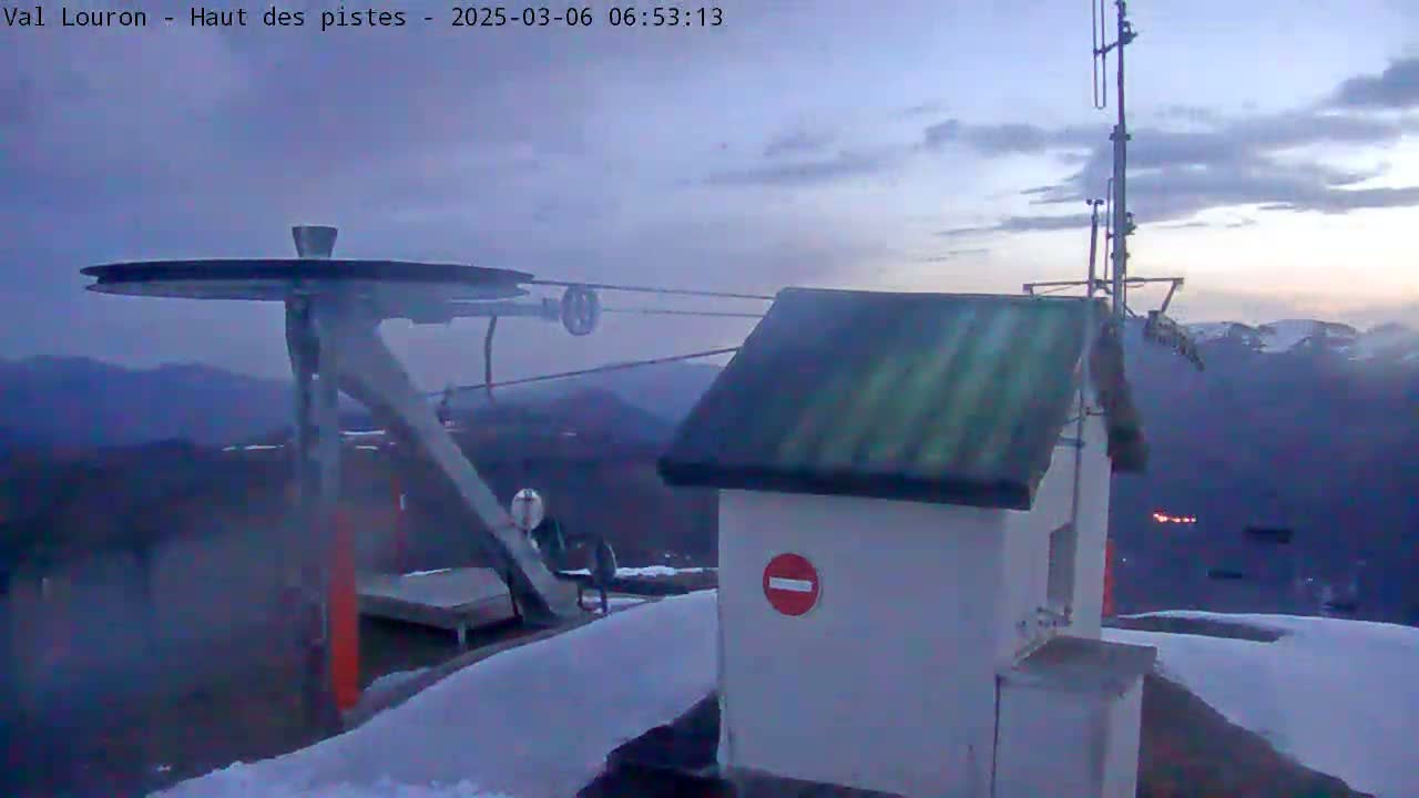 A ski lift pulley system and a small building sit atop a snowy mountain under a twilight sky.