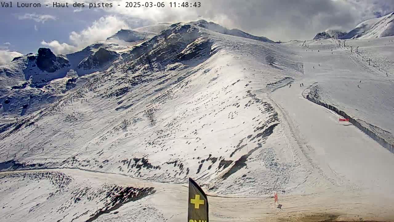A snow-covered mountain slope with several ski runs, under partly cloudy skies.