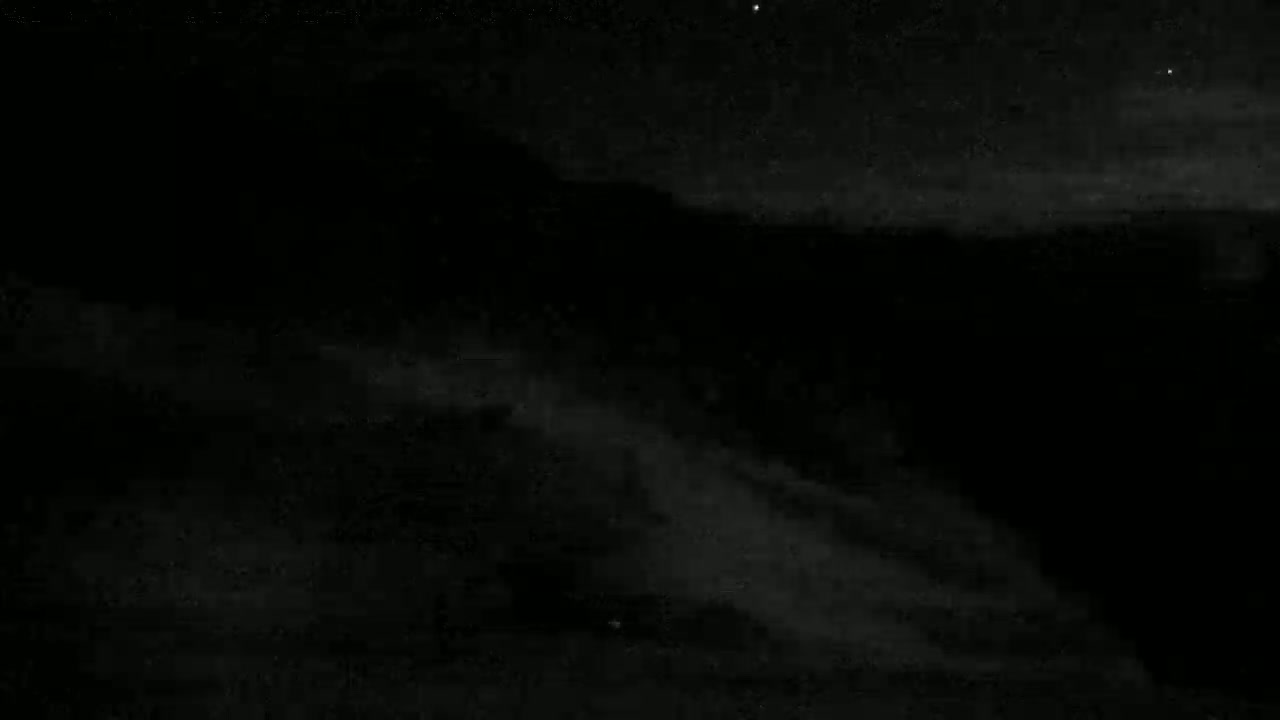A dark, nighttime landscape with low-lying clouds or fog under a mostly clear, starlit sky.
