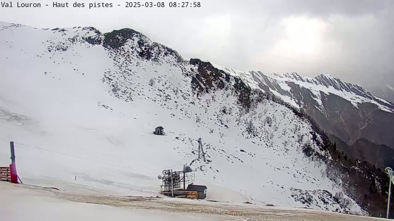 A snow-covered mountain slope with a ski lift and small building is visible under an overcast sky.