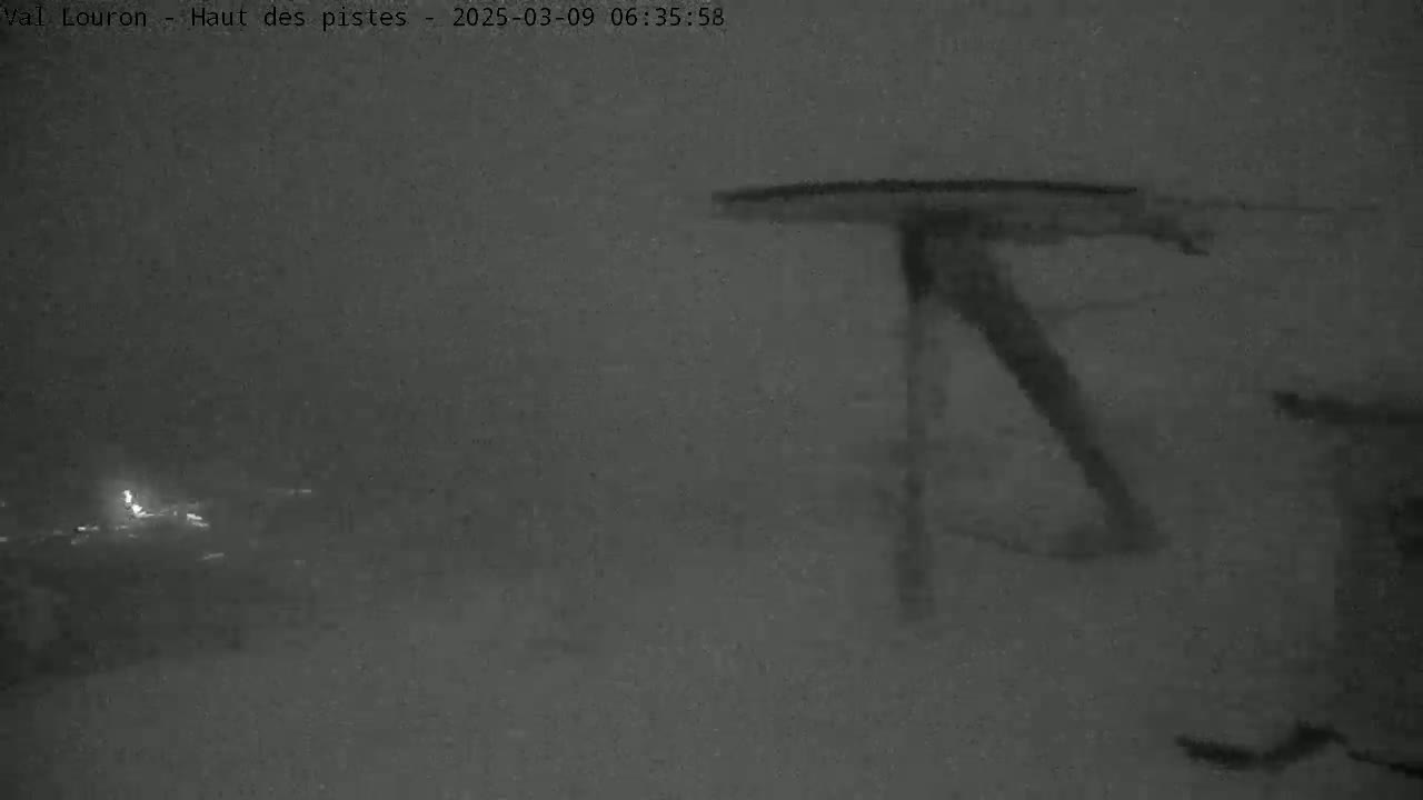 A nighttime, snowy scene shows a tall, dark structure resembling a ski lift against a blurry, snow-covered background.