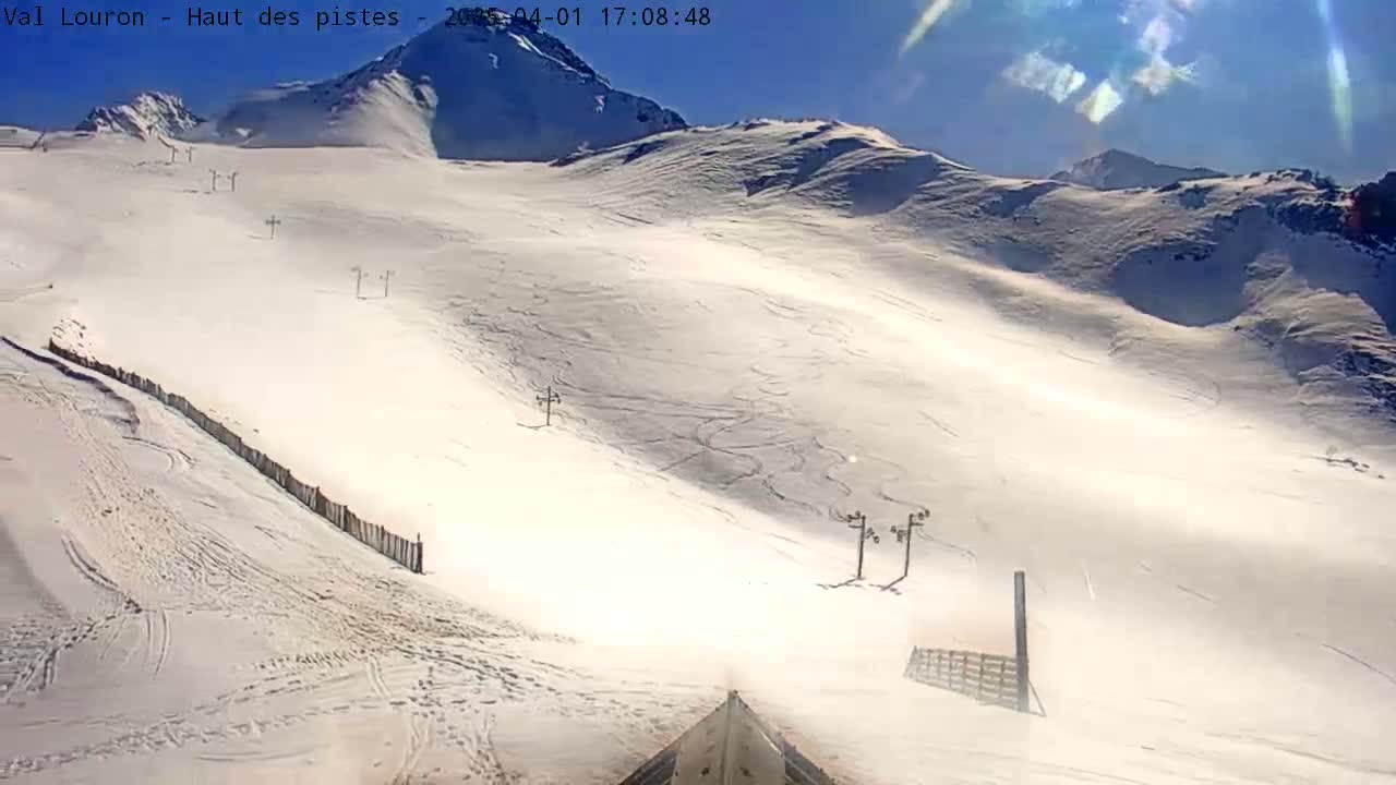 A sunny, snow-covered mountain slope with ski lifts and some ski tracks visible.