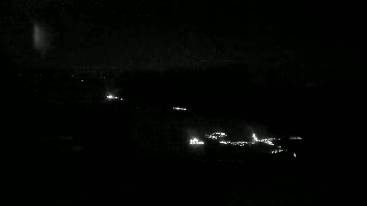 At night, a long stretch of road with sparsely spaced headlights is visible from a high vantage point.