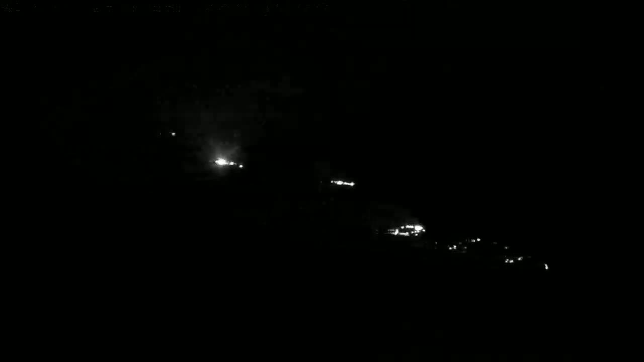 At night, a long line of faint, scattered lights stretches across a dark, seemingly outdoor scene.