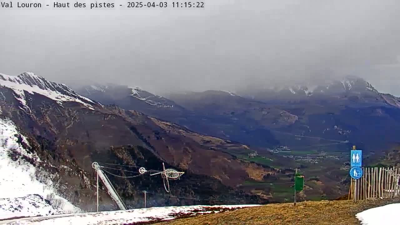 A hazy, overcast view of snow-capped mountains and a valley, with a ski lift and a wooden fence in the foreground.