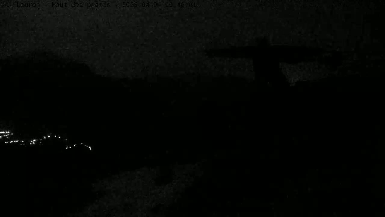 A dark, nighttime scene shows a blurry, indistinct silhouette against a black background, with faint lights visible in the distance.