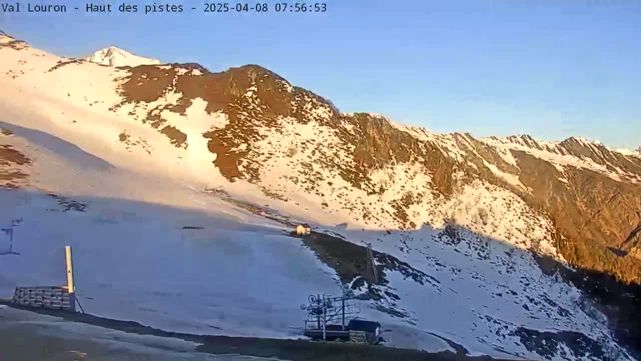 A snow-covered mountainside with patches of brown rock is bathed in the morning sunlight under a clear blue sky.