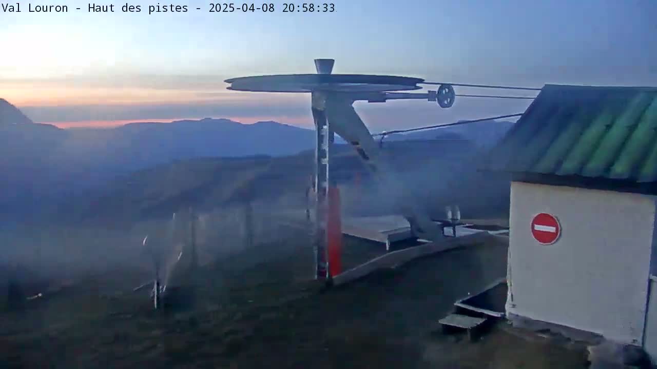 A ski lift pulley system and small building are visible at dusk, with hazy, smoky conditions and distant mountains in the background.