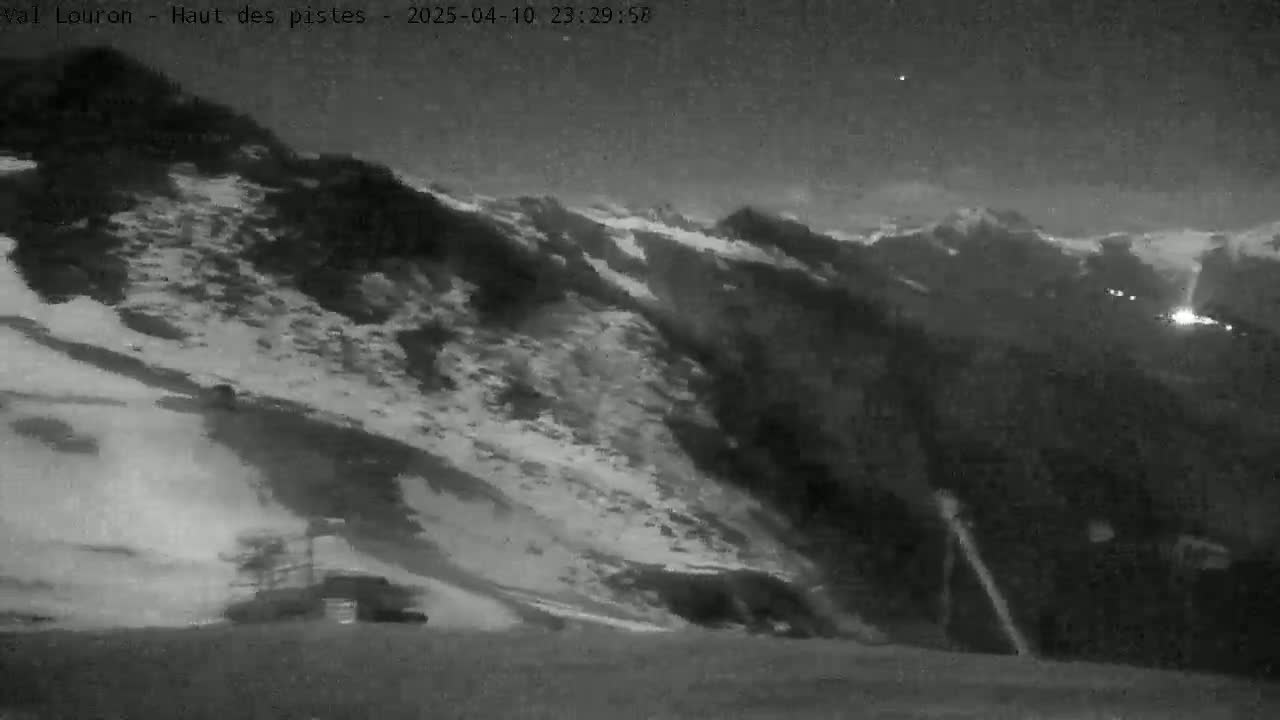A nighttime, snow-covered mountain slope is visible under a mostly clear sky.