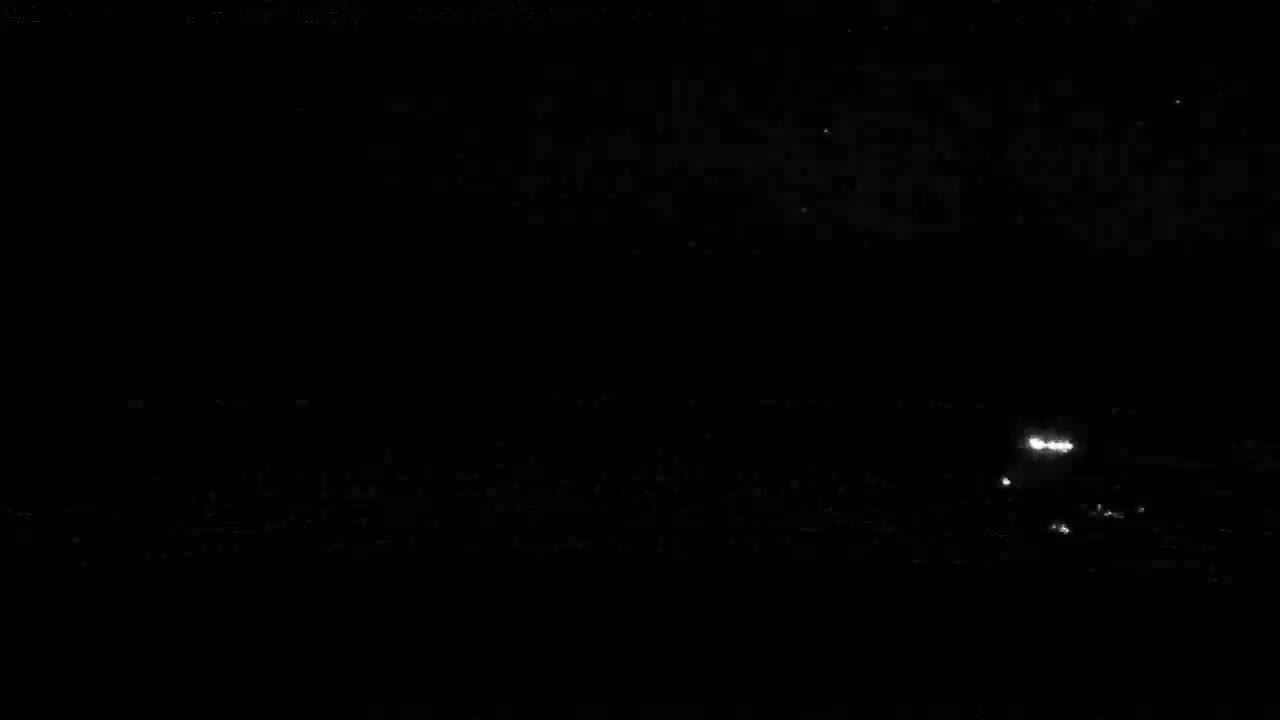 A dark, nighttime scene shows a few bright lights in the distance on a seemingly flat horizon.