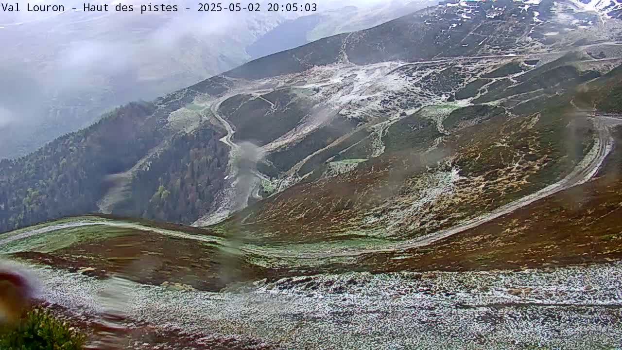 A high-angle view shows winding paths across a snow-dusted mountainside, with some patchy fog in the distance.