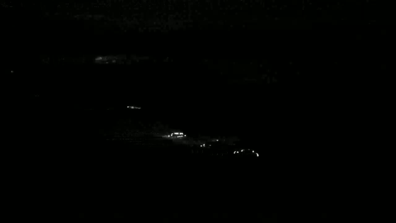 A nighttime, low-light view shows a line of vehicle headlights traveling along a dark road.