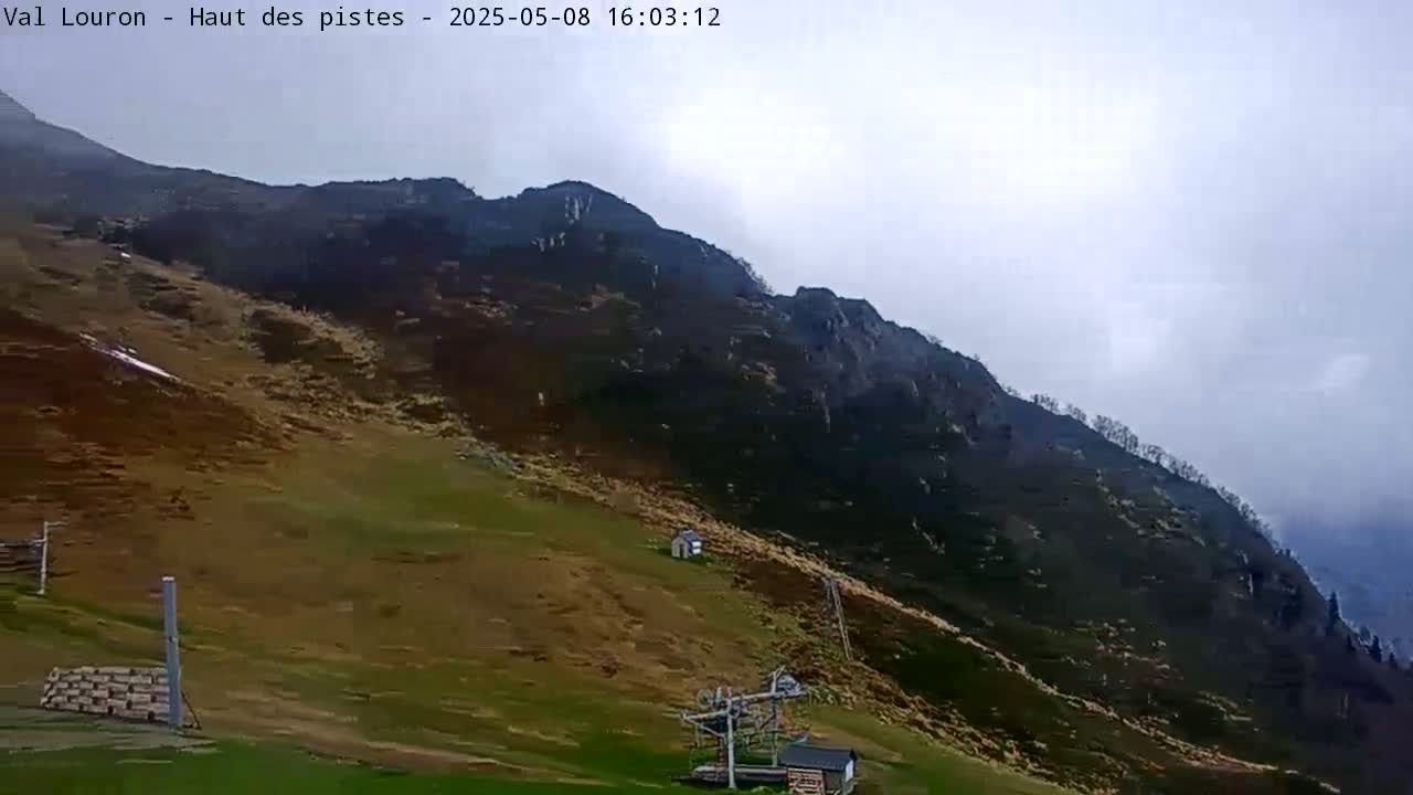 A mostly cloudy day reveals a steep, grassy hillside ascending to a dark, rocky mountain under an overcast sky.