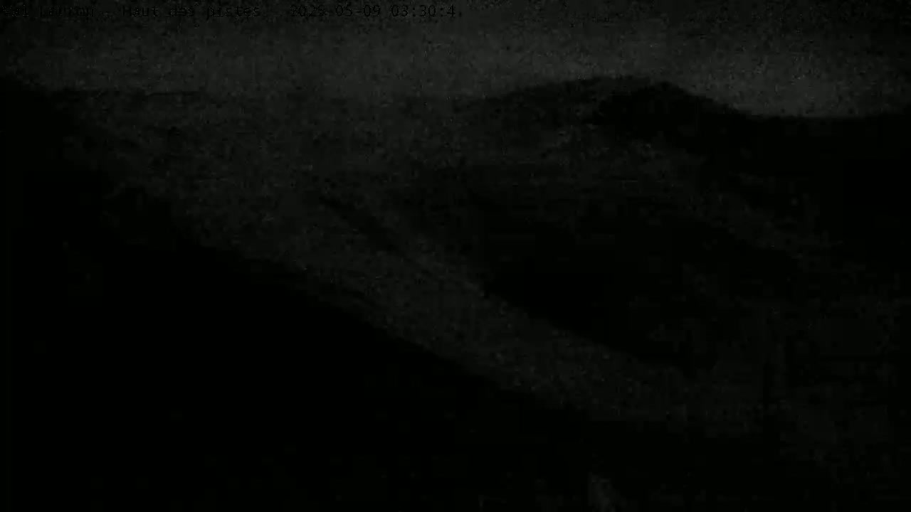 A dark, nighttime view of indistinct, hilly terrain under a cloudy sky.