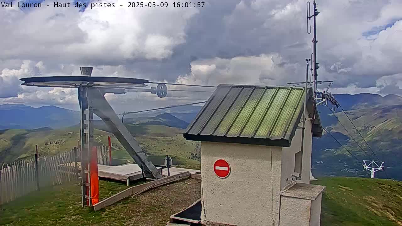 A cloudy mountaintop scene features a ski lift pulley system, a small building, and a distant view of more mountains.
