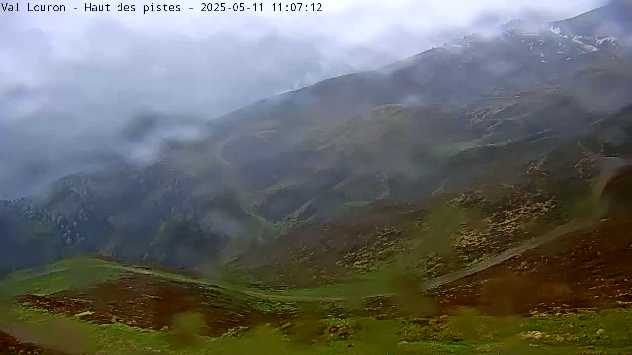 A rain-covered view of rolling green and brown hills shrouded in mist.