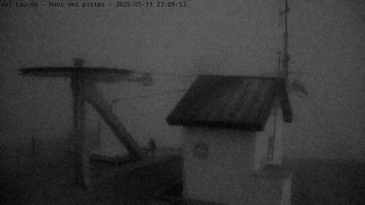 A nighttime, foggy view shows a metal structure next to a small, dark building.