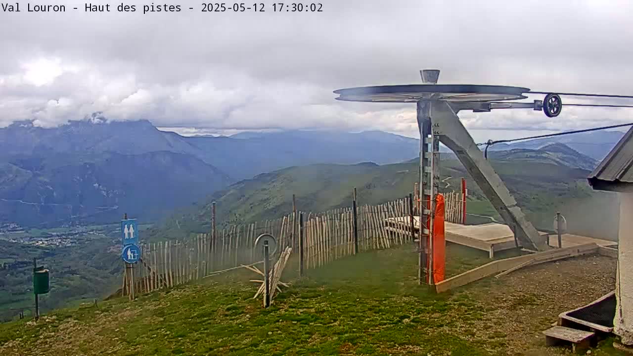 A mountaintop ski lift station on a cloudy day overlooks a valley and distant mountains.