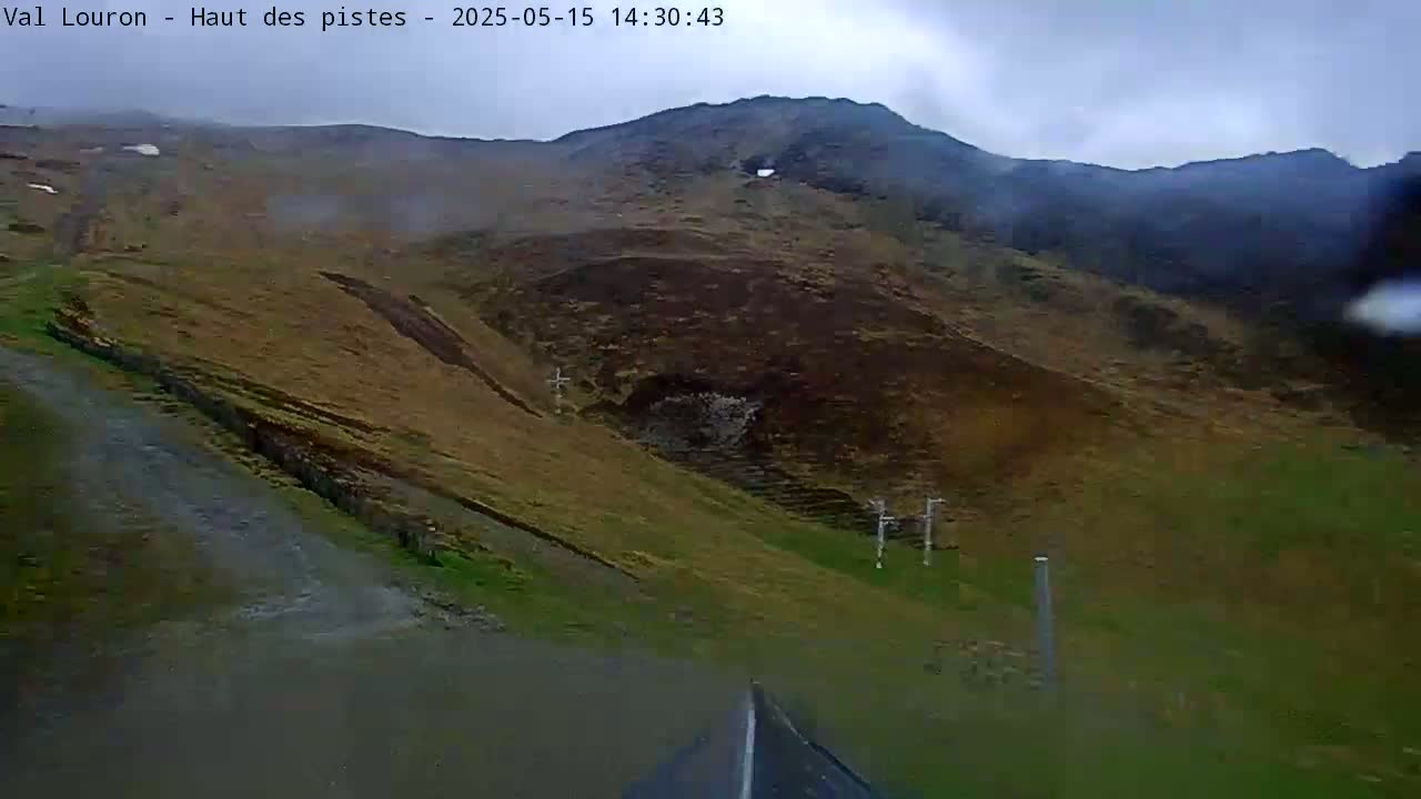 A rain-slicked road winds through a mountainous landscape under an overcast sky.