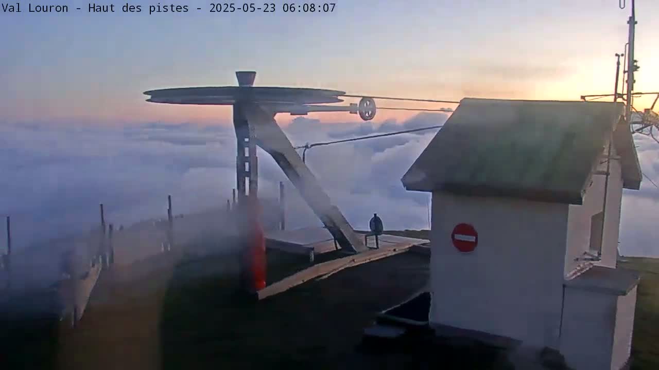 A ski lift mechanism is perched atop a mountain, overlooking a sea of clouds during sunrise.